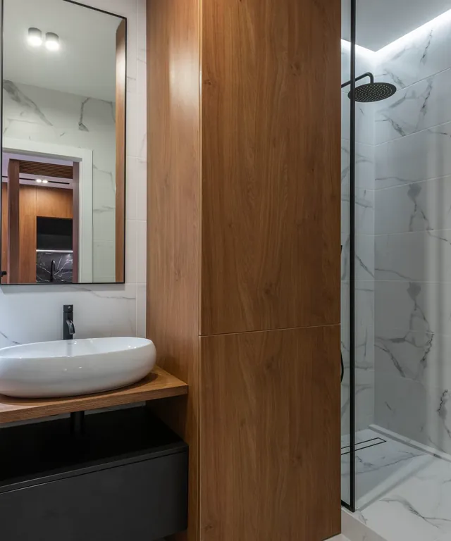 Baño con ducha de cristal, mueble de madera y lavabo sobre encimera