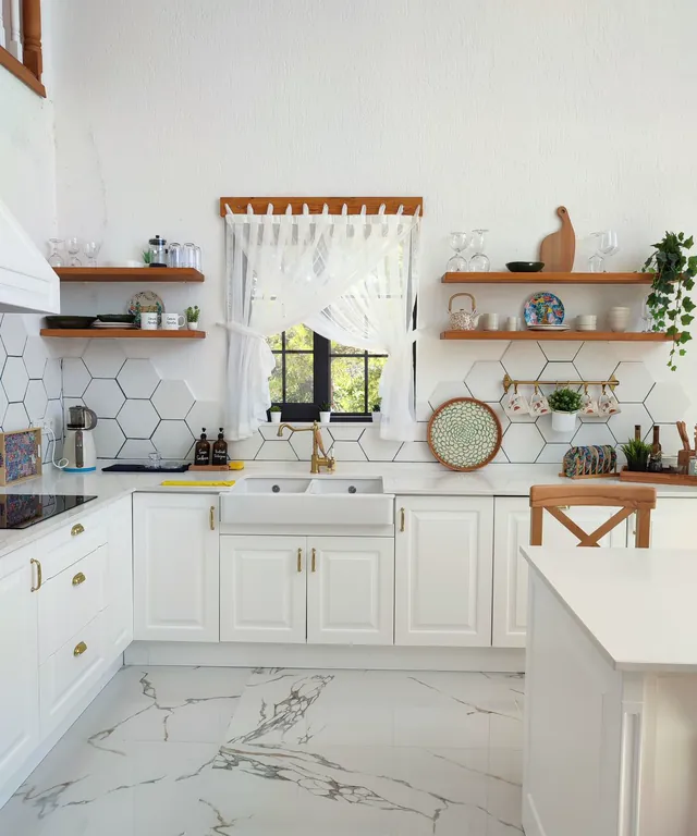 Cocina blanca con suelo de mármol, estantes de madera y una ventana con cortina