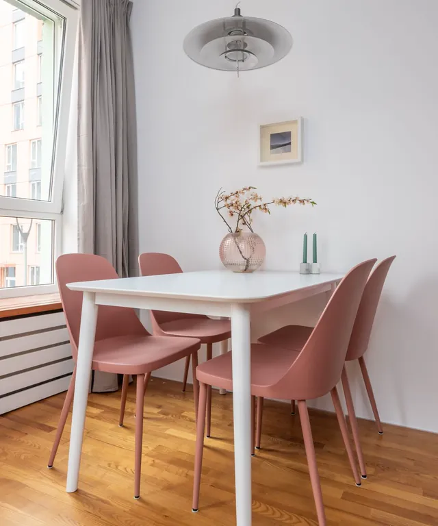 Comedor con mesa blanca y sillas rosas junto a una ventana