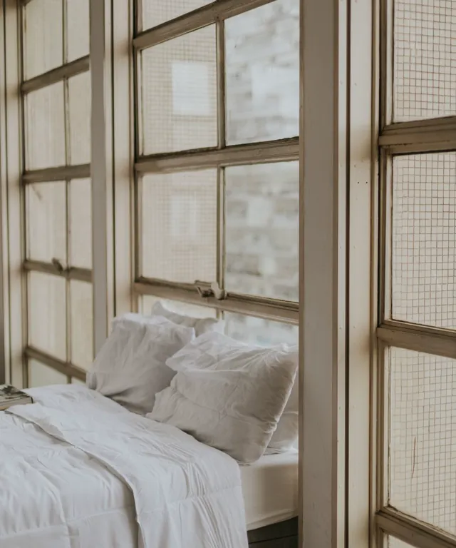 Dormitorio con cama blanca junto a un gran ventanal
