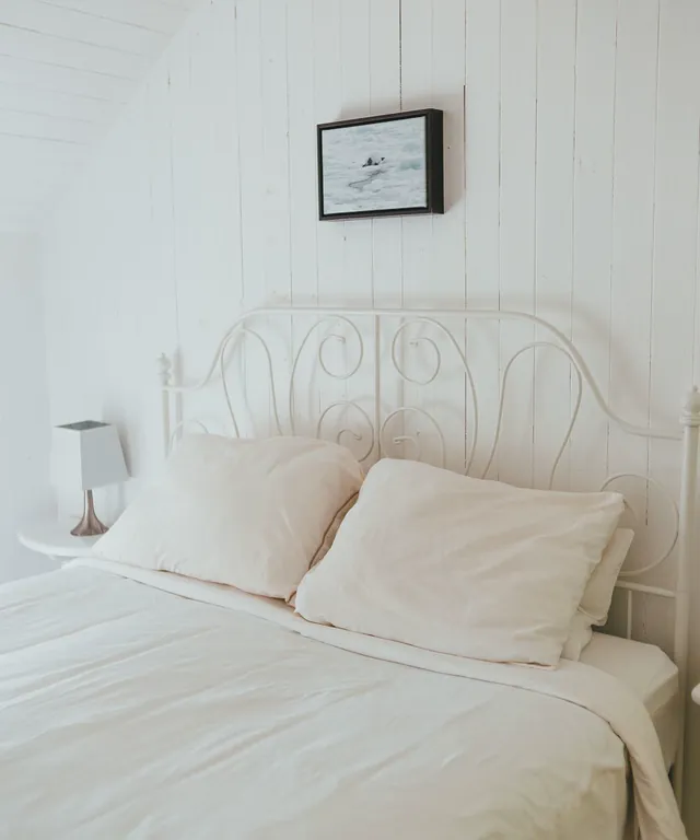 Dormitorio con cama de ropa blanca y cabecero de forja en tonos claros