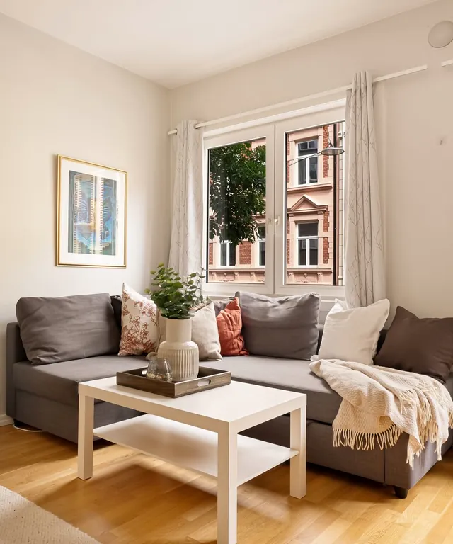Salón luminoso con sofá gris, mesa baja y suelo de parquet junto a una ventana